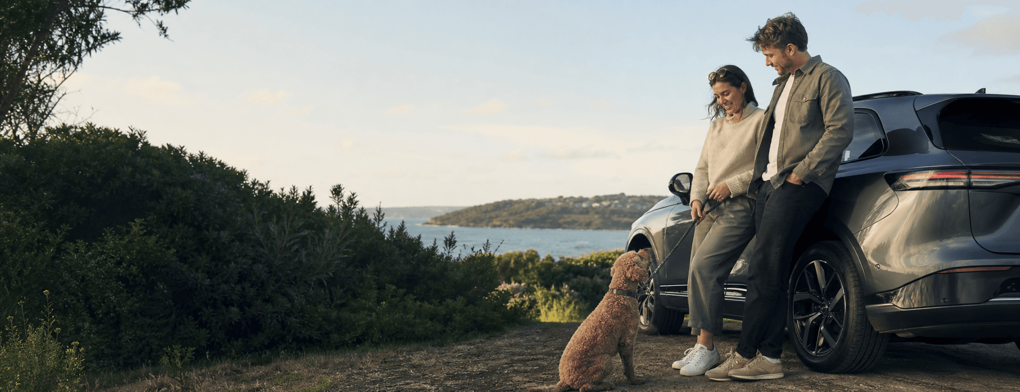 A couple with their dog beside a car at an Australian coastal lookout