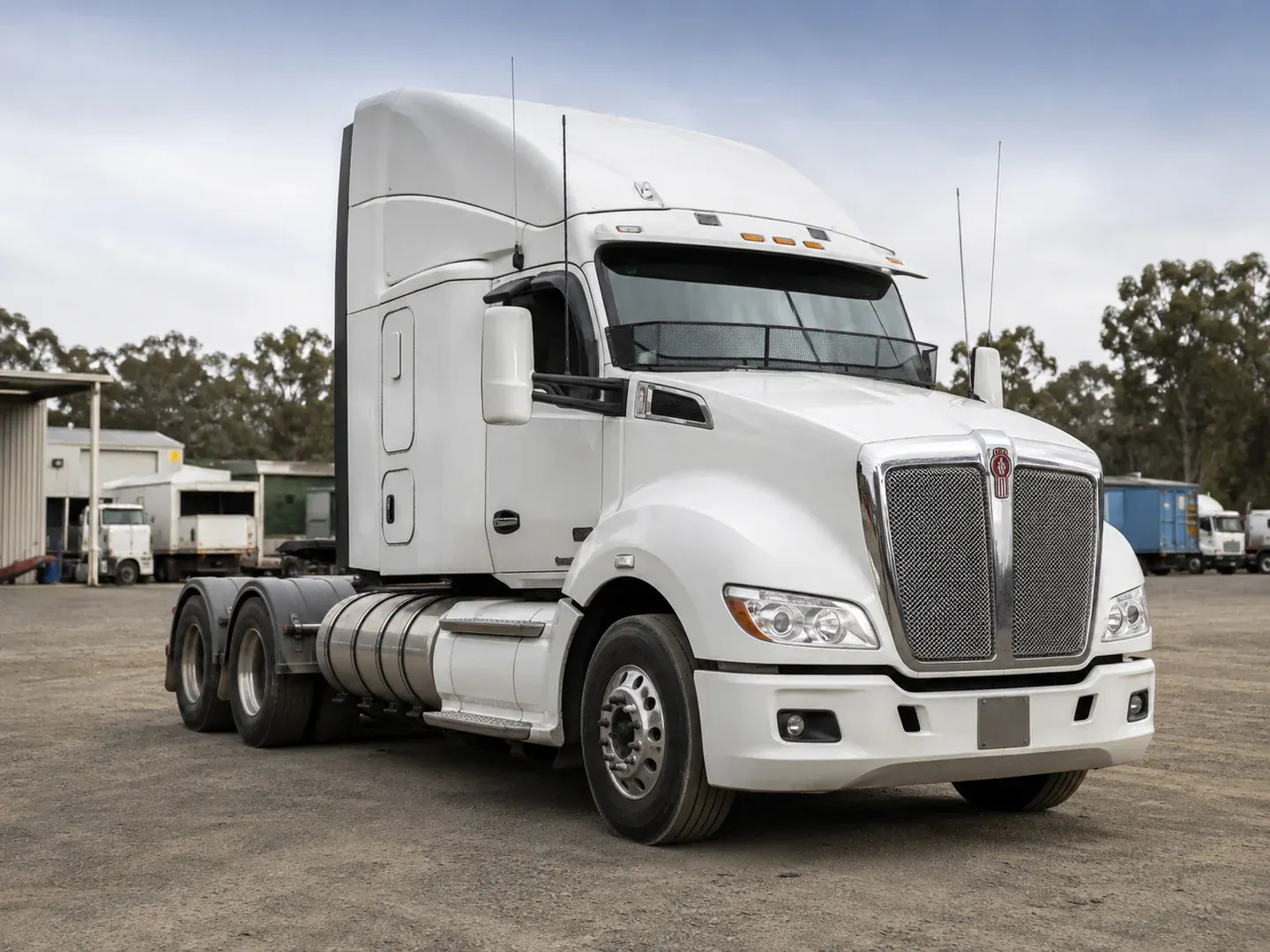 Illustrative scene: An accurate 2023 Kenworth T610 prime mover parked at a modest Australian interstate transport depot, conventional aerodynamic bonnet, Kenworth badge, white cab with sleeper, no trailer so complete truck visible in three-quarter view. Not the actual customer or their asset.