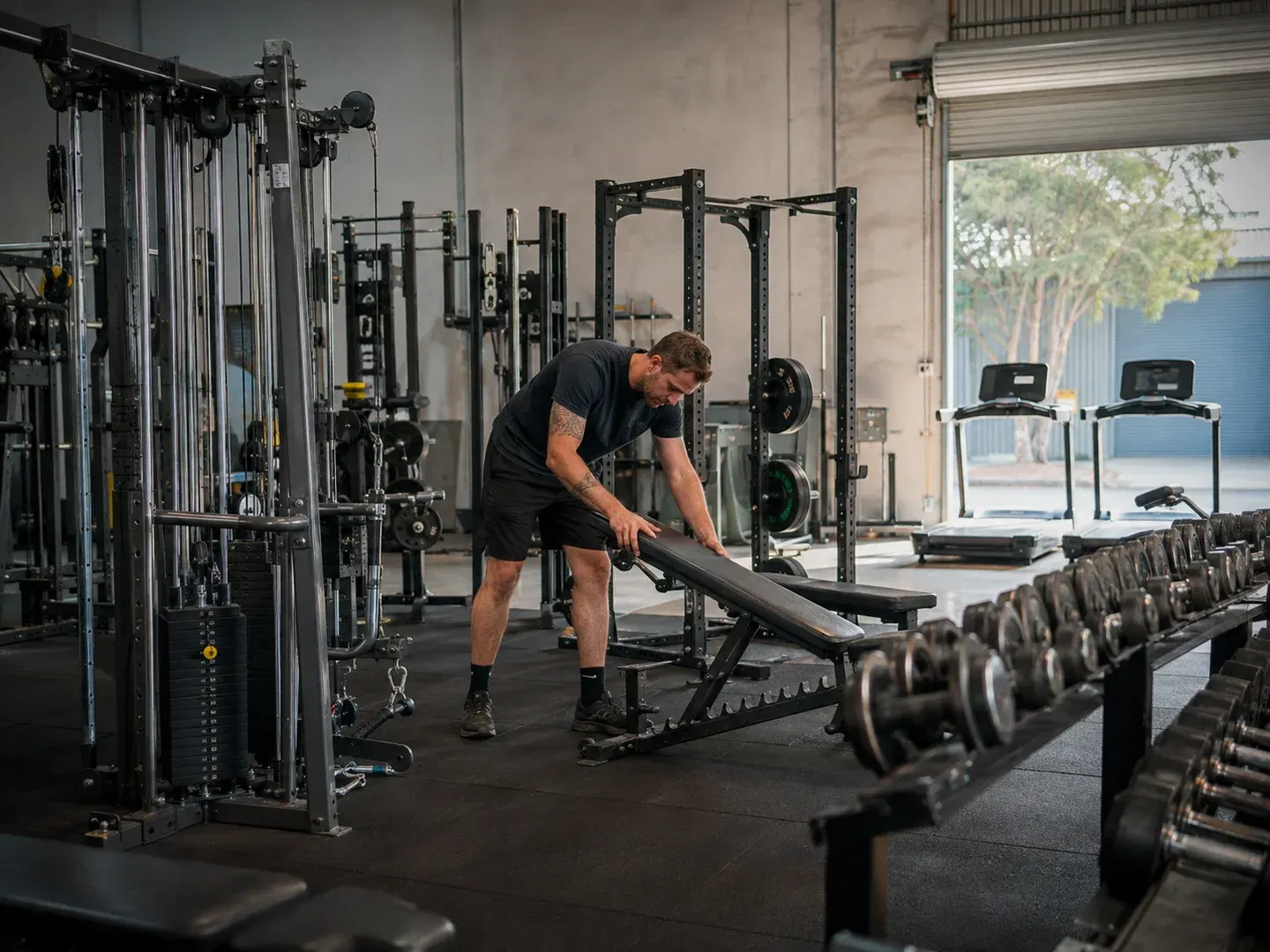 Illustrative scene: An Australian independent gym fitting out a larger industrial unit with used commercial strength and cardio equipment: cable station, squat rack, dumbbell racks and two treadmills. Not the actual customer or their asset.