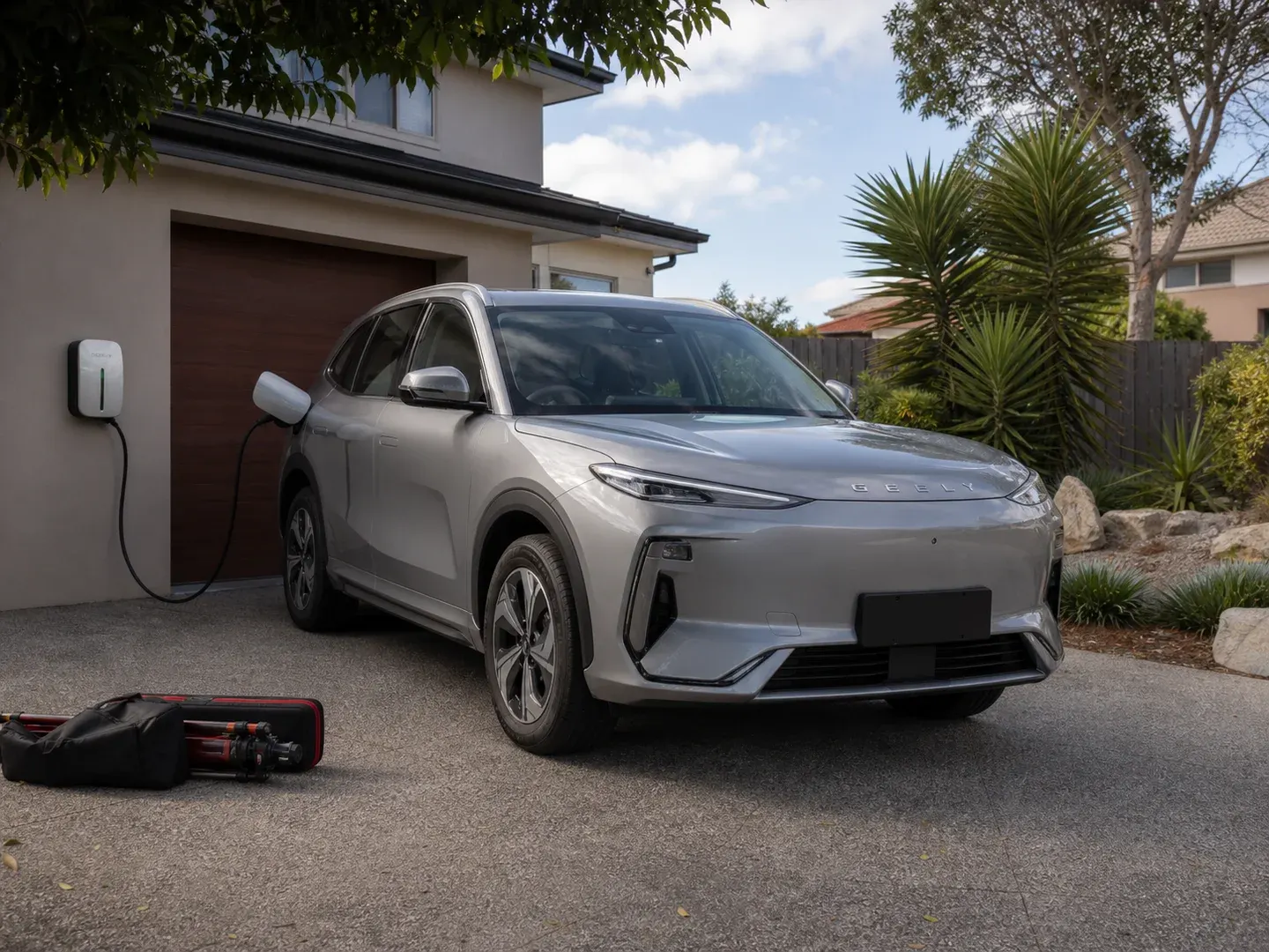 Illustrative scene: A contemporary Geely electric SUV at an ordinary Australian residential EV charger, recognisable Geely badging and realistic production vehicle design, calm silver body, front three-quarter view. Not the actual customer or their asset.