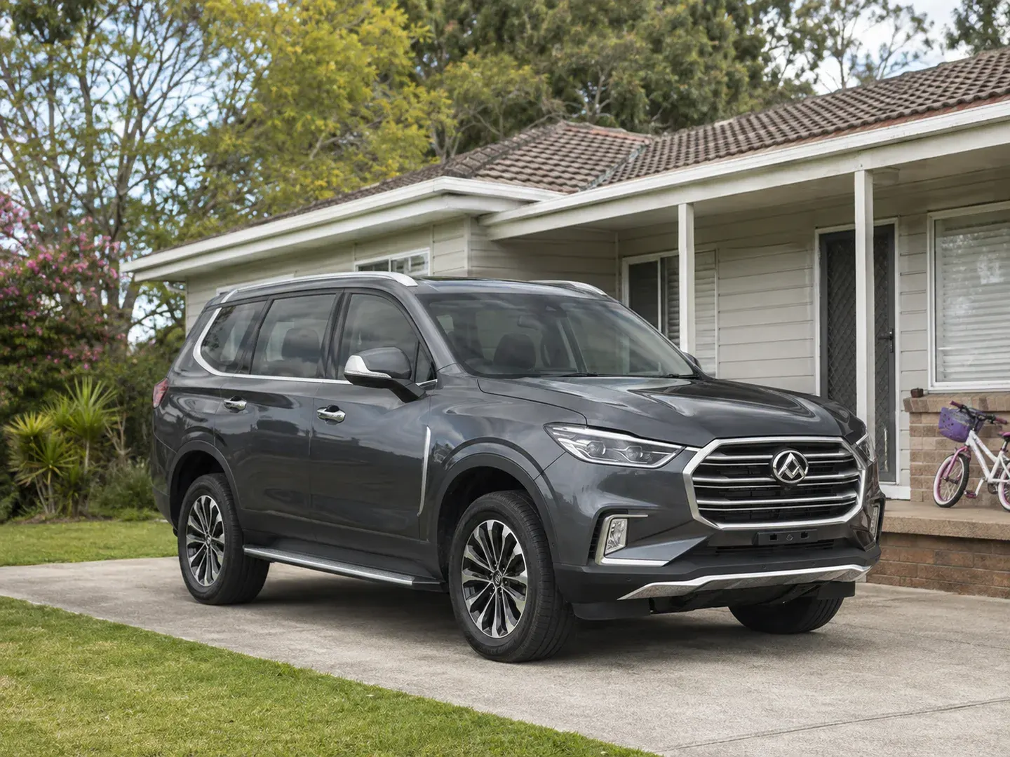 Illustrative scene: A new LDV D90 family SUV parked in the driveway of a modest Australian suburban home, a child's bicycle beside the porch. Not the actual customer or their asset.