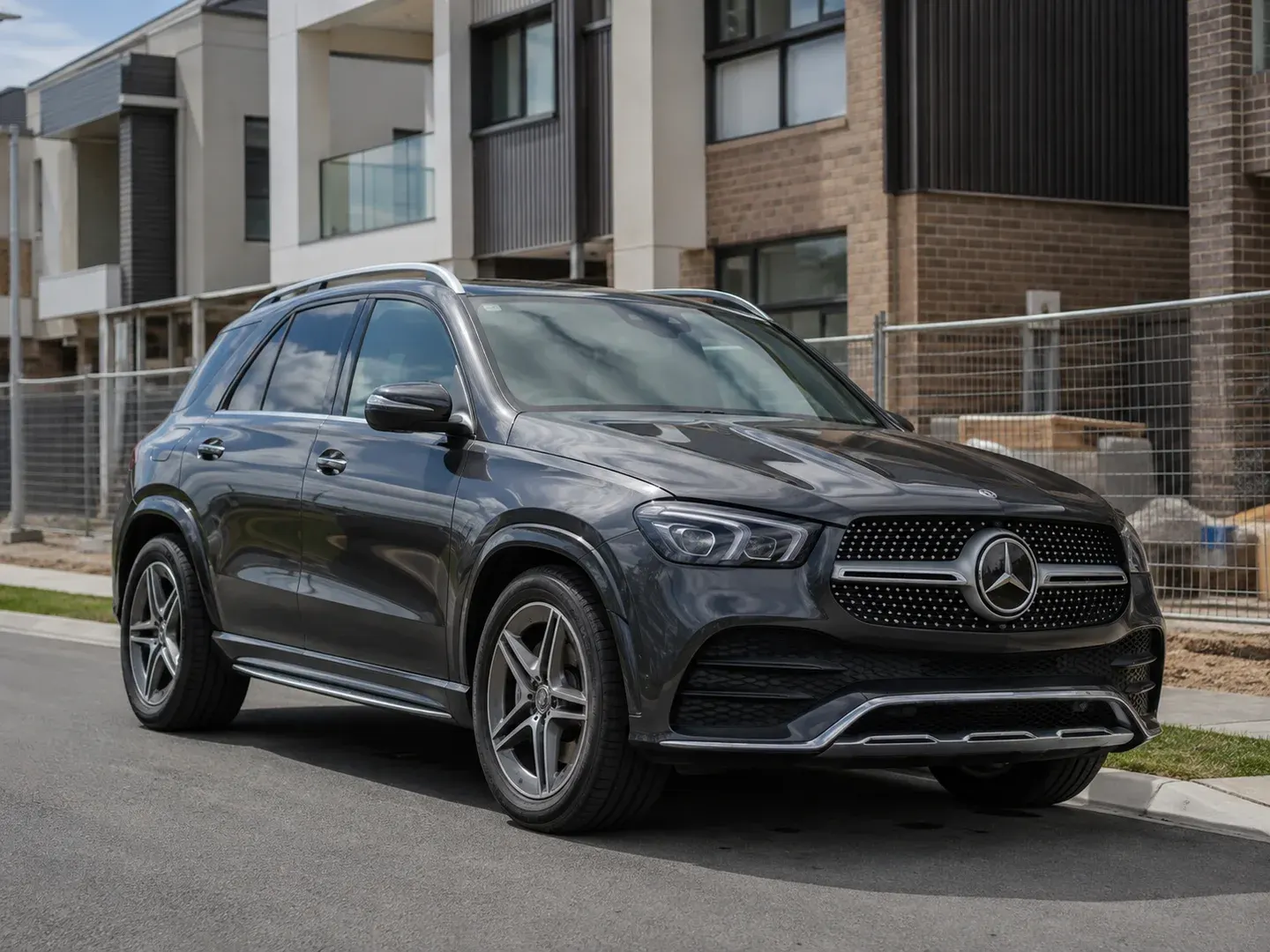 Illustrative scene: A 2026 Mercedes-Benz GLE SUV parked outside an Australian residential property development nearing completion, recognisable Mercedes grille star and accurate GLE silhouette, charcoal metallic paint, complete vehicle in three-quarter front view. Not the actual customer or their asset.