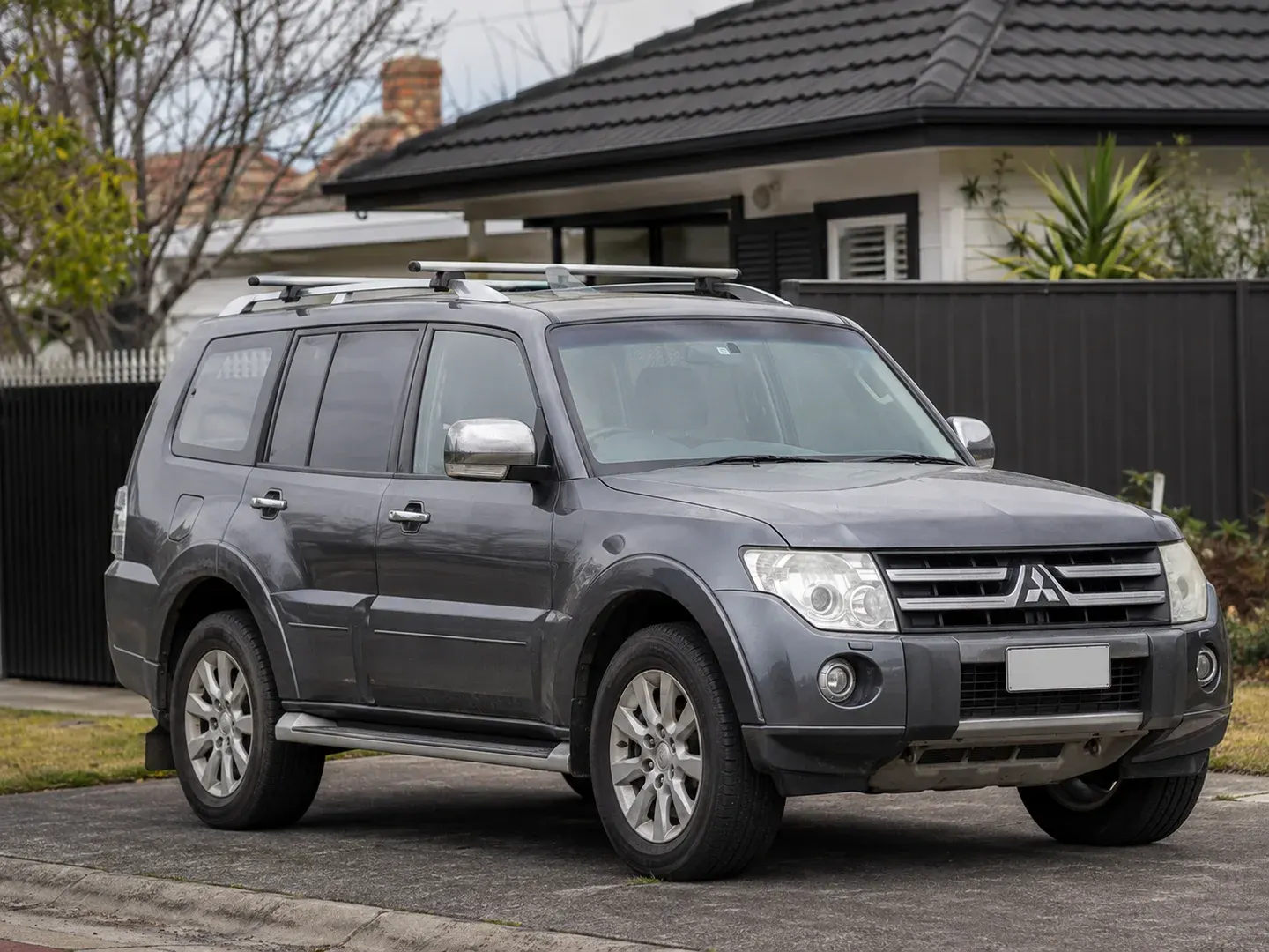 Illustrative scene: A used 2014 Mitsubishi Pajero five-door 4WD parked outside a modest Melbourne home, accurate boxy fourth-generation Pajero body and Mitsubishi badge, light wear, front three-quarter view with whole vehicle visible. Not the actual customer or their asset.
