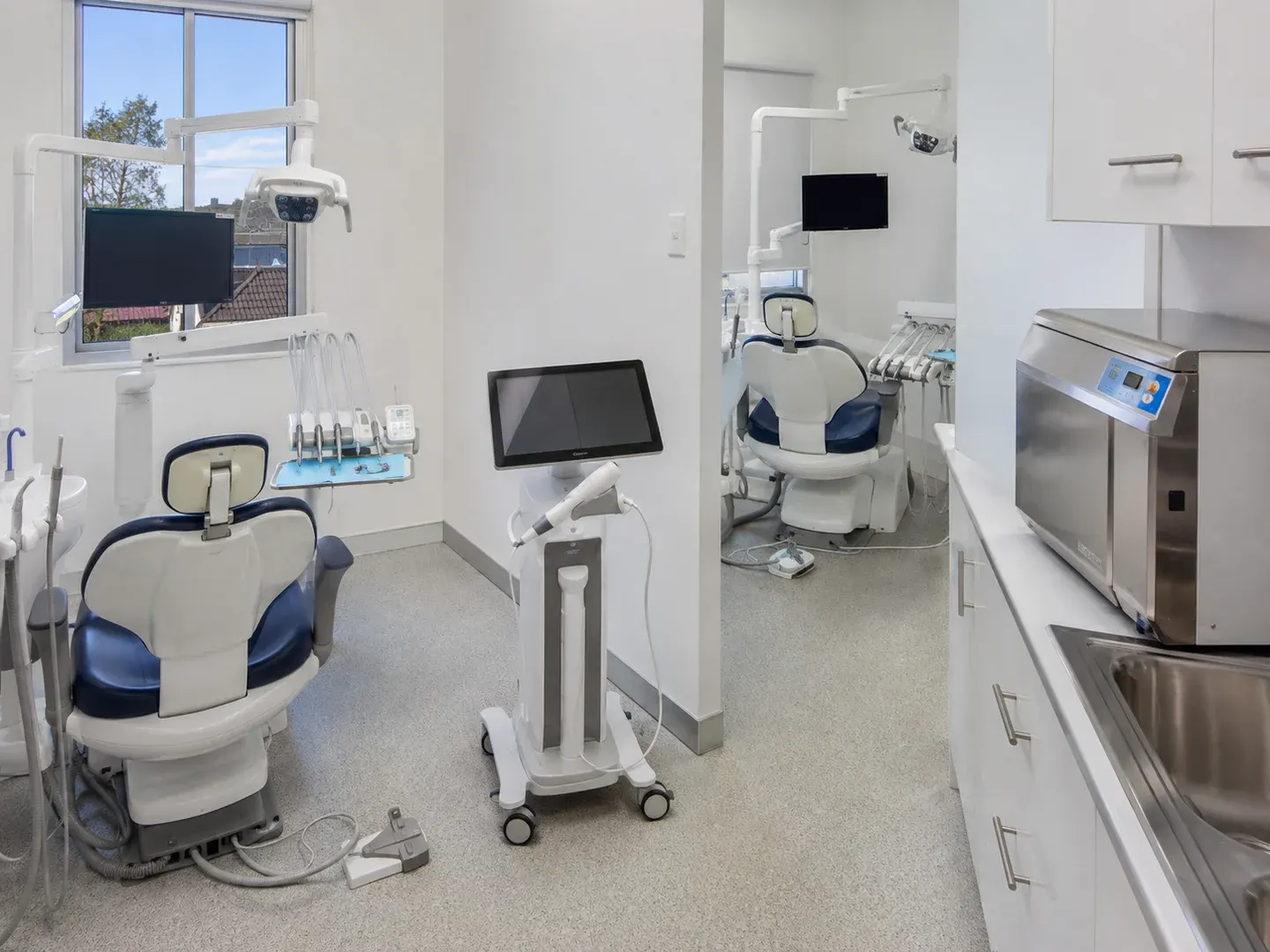 Illustrative scene: A modest newly equipped Australian dental practice with exactly two refurbished dental chairs in adjacent treatment bays, an intraoral scanner on a wheeled stand and a stainless steriliser visible on the side bench. Not the actual customer or their asset.